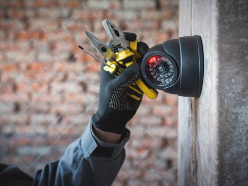 Security camera on the wall close up and worker hand with a work tools. Video surveillance system maintenance concept.